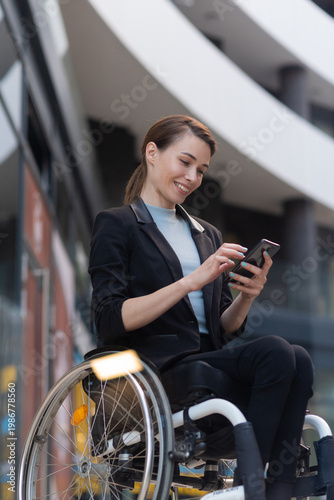 Smiling businesswoman in wheelchair using smart phone outside