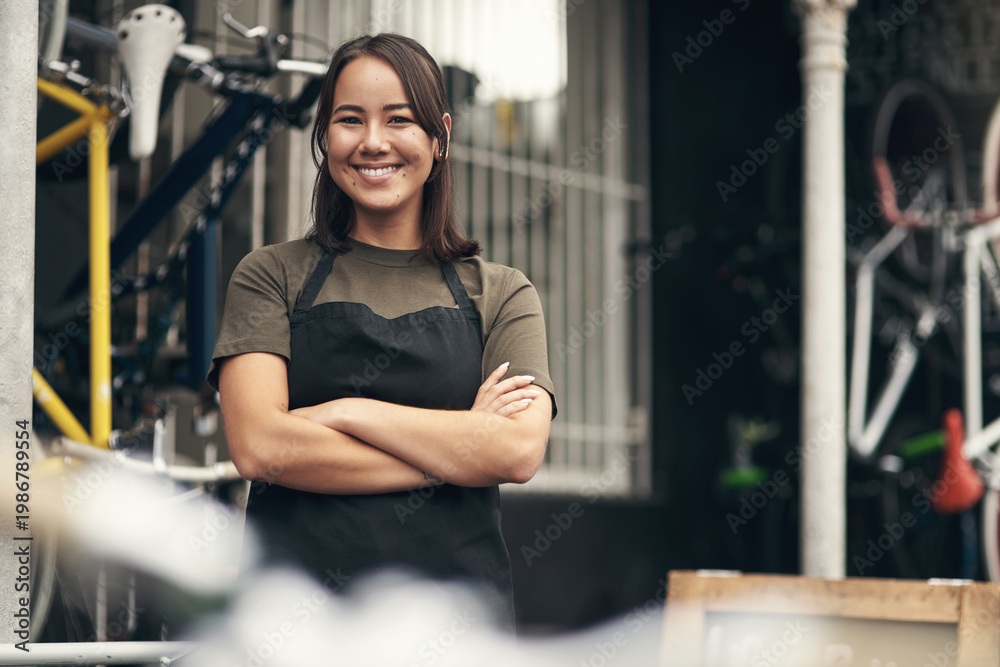Fototapeta premium Woman, happy and arms crossed at bicycle shop in portrait with pride, confidence and small business. Asian person, smile and mechanic for bike maintenance services, gear and job at garage in Cambodia