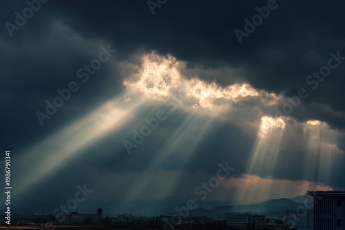 Dramatic crepuscular rays shining through dark storm clouds over a city skyline, sunbeams breaking through the sky at sunset.