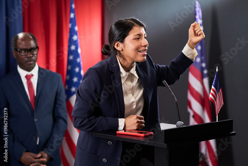Canvas Print Medium shot of Latin young adult politician speaking at podium and raising fist during campaign event, conveying leadership and civic engagement