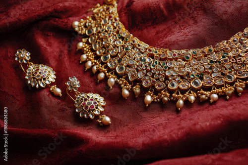 Close up of ornate indian bridal jewelry set including gold necklace, earrings and maang tikka arranged on red silk fabric, soft studio lighting, ultra-sharp focus in simple