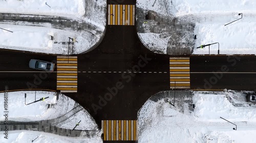 At an intersection on a winter road, two cars turn left one after the other. Pedestrian crossings at each road intersection. Aerial view from a drone. Winter road snow. High quality 4k footage