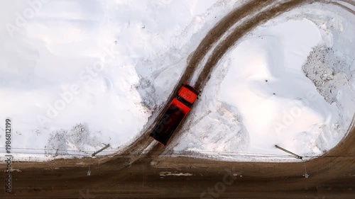A large dump truck construction truck is moving along an unpaved snowy road top view. Winter transport truck. Red truck snow . High quality 4k footage