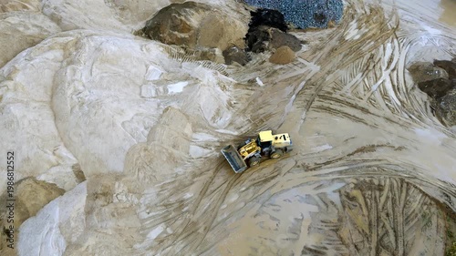 A large yellow tractor working in a sand pit view from a quadcopter from a height. Sand pits large K construction machinery moves the soil. High quality 4k footage