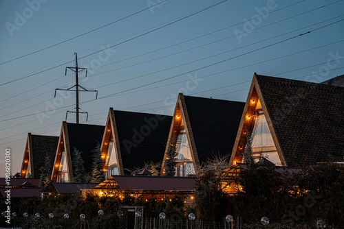 A row of beautifully illuminated A-frame cabins under a twilight sky, showcasing modern architecture and cozy ambiance, perfect for a relaxing getaway.