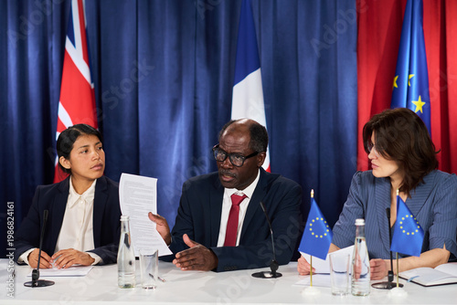 Canvas Print Medium shot of diverse business leaders reviewing document during international press conference, discussing policy alignment