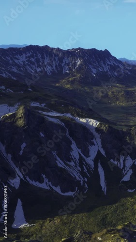 The scene shows mountains with rocky slopes and valleys under a clear sky. Snow is visible on some peaks. The landscape appears vast and open. Light touches the terrain, revealing details.