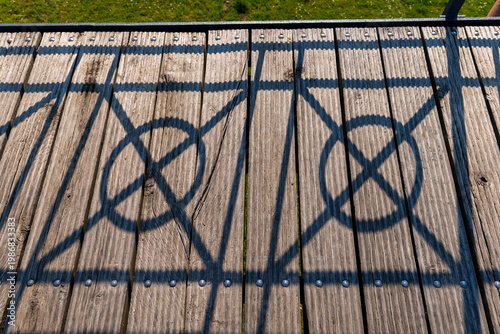 Wooden deck casting intricate shadows of patterns, sunlight creating a visual play outdoors in a serene park setting