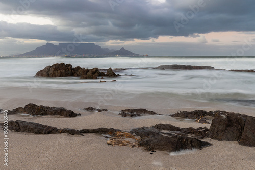 An amazing view from Bloubergstrand beach on the famous table mountain in Cape Town, seen during a colourful sunrise with a amazing dramatic cloudscape and waves braking on the coast from the rough At