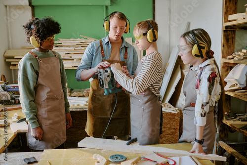 Obraz na plátně Teenagers learning woodworking, operating electric jigsaw with instructor guidance in workshop