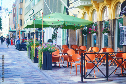 Cuadro en lienzo Charming outdoor cafe terrace with orange chairs, green umbrellas and flower pla