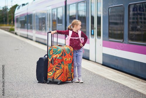Happy young girl standing with colorful suitcases on a train platform in Finland, ready for travel and family trip by rail