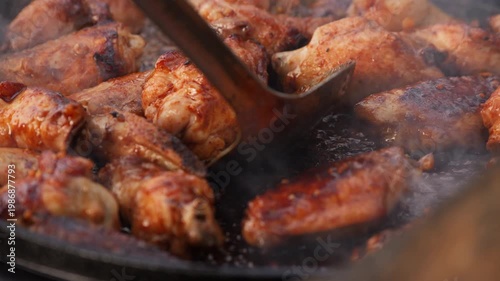 Roasted chicken wings in BBQ sauce cooking on a hot skillet, chef stirring juicy meat with smoke and steam.