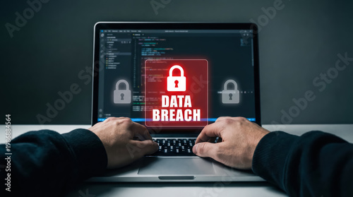 Hacker hands typing on a laptop keyboard with a digital data breach warning symbol on the screen