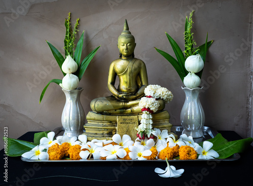 Golden Buddha statue decorated with fresh jasmine garland, white lotus flowers, and frangipani on a tray for worship.