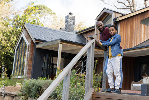 African American father with boy standing on porch stairs leaning on cable railing, copy space