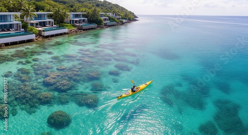 Person kayaking in turquoise water near coastal villas. An aerial shot conveying serenity and adventure. Tropical getaway, luxury travel, water sport.