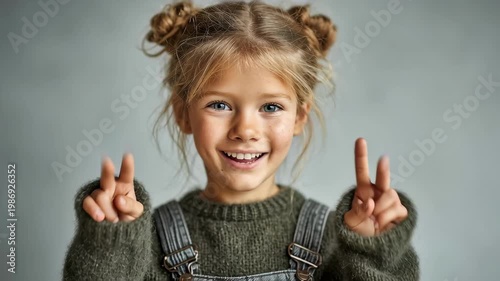 Portrait of a happy young Caucasian girl with hair buns making peace signs and smiling in a studio.