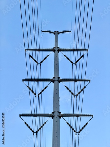 Low angle view of a high-voltage power transmission tower with multiple wires against a clear blue sky.