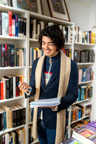 Fotografia Young man smiling while browsing book collection in a second-hand bookstore