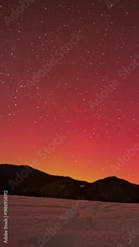Vertical time lapse of red aurora borealis and stars over winter mountain landscape