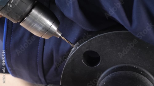 Worker manually drilling a hole in a metal part using a hand drill