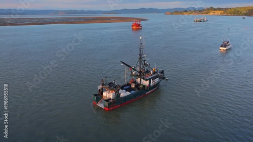 A fishing trawler with crates of catch on the water near a sandbar and distant hills in Kawhia Harbour, Kawhia, Waikato, New Zealand The vessel is preparing to moored.