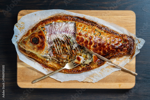 Traditional carp coulibiac fish pie in fish shape, closeup. Baked fish coulibiac pie shaped like a fish filled with carp and mushrooms on a wooden board. Traditional gourmet seafood pastry concept