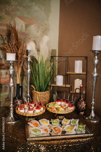 Luxury dessert table for a boy's birthday with panna cotta, colorful cake pops, and rustic decor. Elegant candy bar featuring silver candlesticks, pampas grass, and golden trays.