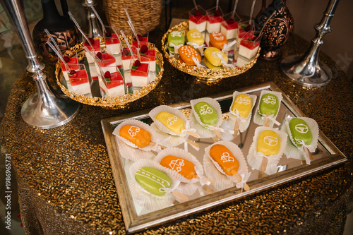 Luxury candy bar with cake pops decorated with cars and tractors, and raspberry panna cotta. Festive desserts on golden trays for a boy's birthday party with copy space.