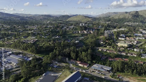 Drone lowers in wide shot of neighborhood north of city in the late afternoon before sunset in mountain town of Mbabane, Eswatini