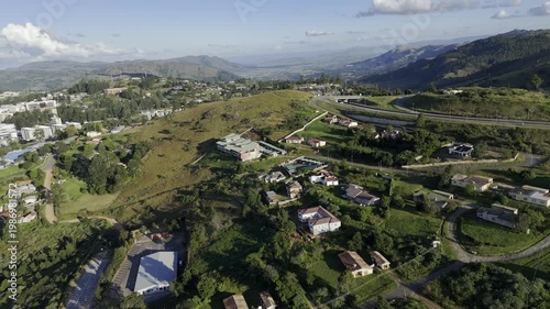 Drone facing south, orbits left as highway cuts through hills in the late afternoon before sunset in mountain town of Mbabane, Eswatini
