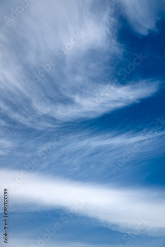 Delicate wisps of cloud on a sunny day with a blue sky. A natural, monochrome weather background. Beautiful weather with light cloud cover and sunshine.