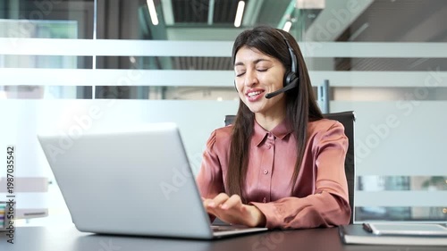 Female call center operator wearing headset working in office, talking to client via laptop. Corporate support agent providing customer assistance on helpline, communication, service, professionalism.