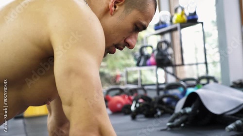 Focused athletic man performing intense workout on gym floor, showcasing strength and determination through progressive motion, surrounded by fitness equipment and vibrant atmosphere