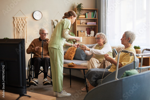 Φωτογραφία Wide shot of female caregiver serving drinks to senior residents in nursing home