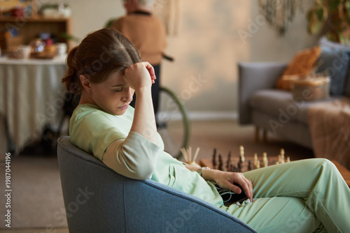 Fotografie Middle aged Caucasian female caregiver sitting with head in hand in nursing home