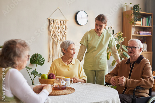 Фотография Senior caregiver assisting elderly residents during tea time in nursing home, su