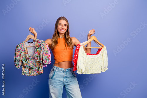 Tableau sur toile Young stylish woman holds colorful tops and smiles during fashion shopping photo