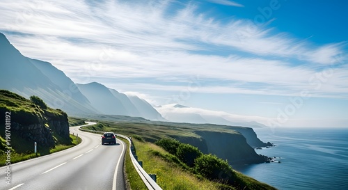 Dramatic coastal road winding along steep cliffs overlooking the ocean, with a car driving towards the horizon under a bright blue sky with wispy clouds.