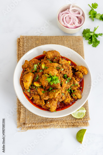 Authentic Indian Chicken Curry in White Bowl with Coriander, Onion and Lime on Rustic Background, Overhead Vertical Composition