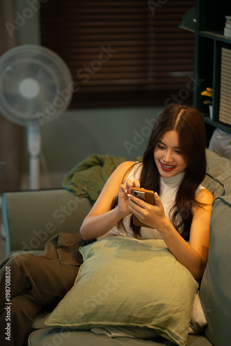 Konstfotografi Young woman browsing on smartphone while sitting comfortably on sofa at home