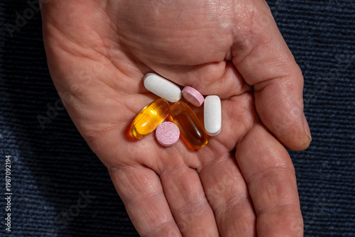 Assorted pills and capsules in a human hand, closeup. Hand holding various pills tablets and gel capsules. Concept of healthcare medical treatment daily medication or supplement intake for wellness