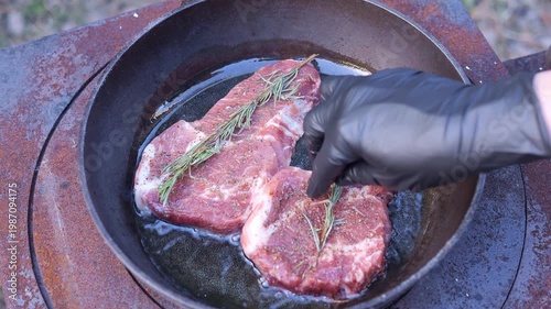 Rustic outdoor cooking meat on hot pan over fire meat frying with rosemary and spices Traditional village cooking shows meat preparation culture countryside lifestyle and authentic food tradition