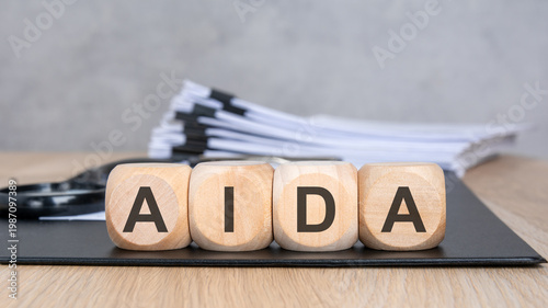 AIDA acronym on wooden blocks. Blurred background with a document stack and magnifying glass. Marketing and sales funnel concept.