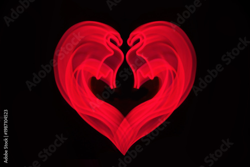 Neon pink flamingo LED lamp in shape of heart on black. Blurred abstract background.