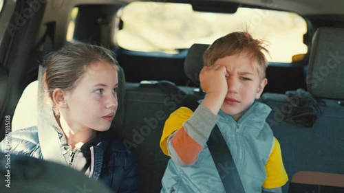 Tired little boy rubbing eyes in car with sister