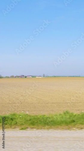 Car side window view of road next to a farm land