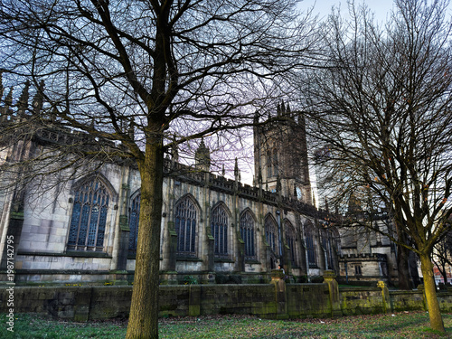 Manchester, UK cathedral exterior with gothic architecture, stone tower and leafless trees in a winter urban park