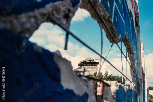 Historisches Foto, Blick durch die Mauer auf das Denkmal eines sowjetischen Panzers am ehemaligen Checkpoint Bravo, Berlin, 1990